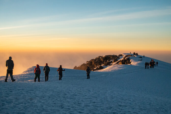 Bergsteiger am Gipfelplateau des Kilimanjaros bei Sonnenaufgang